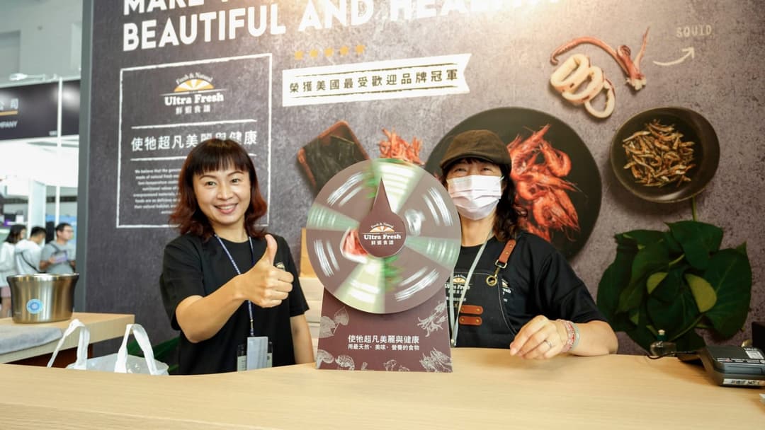 兩位工作人員在展位櫃檯後方比讚