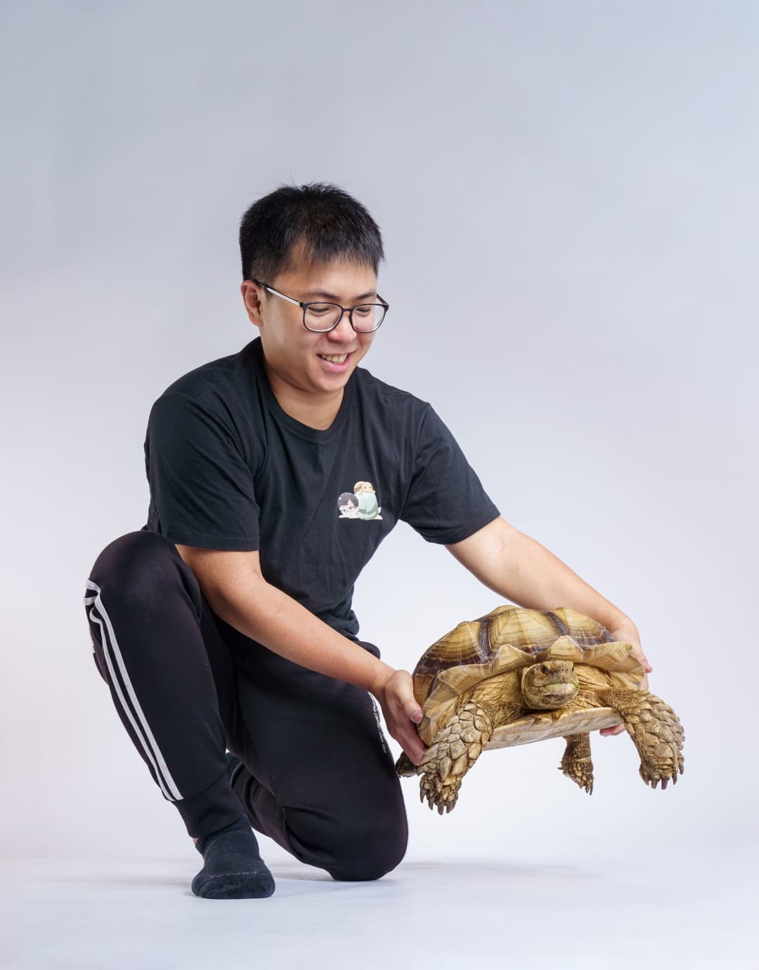 九桃蹲在白色背景前,手裡抱著一隻陸龜